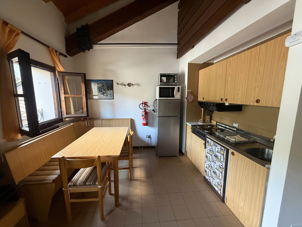 Cucina attrezzata con tavolo e panca in legno, illuminata dalla finestra