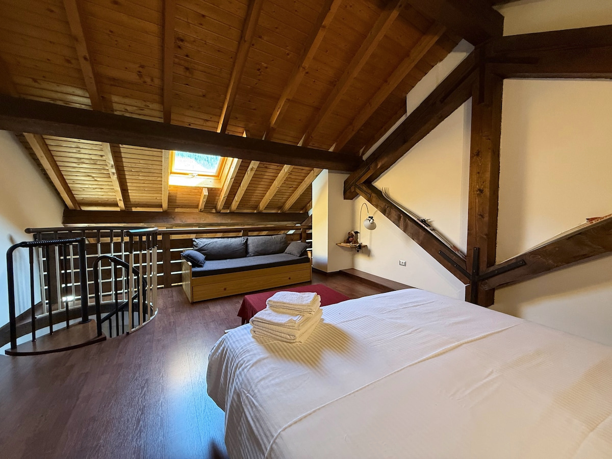 Letto matrimoniale con asciugamani e vista sul resto della camera mansardata