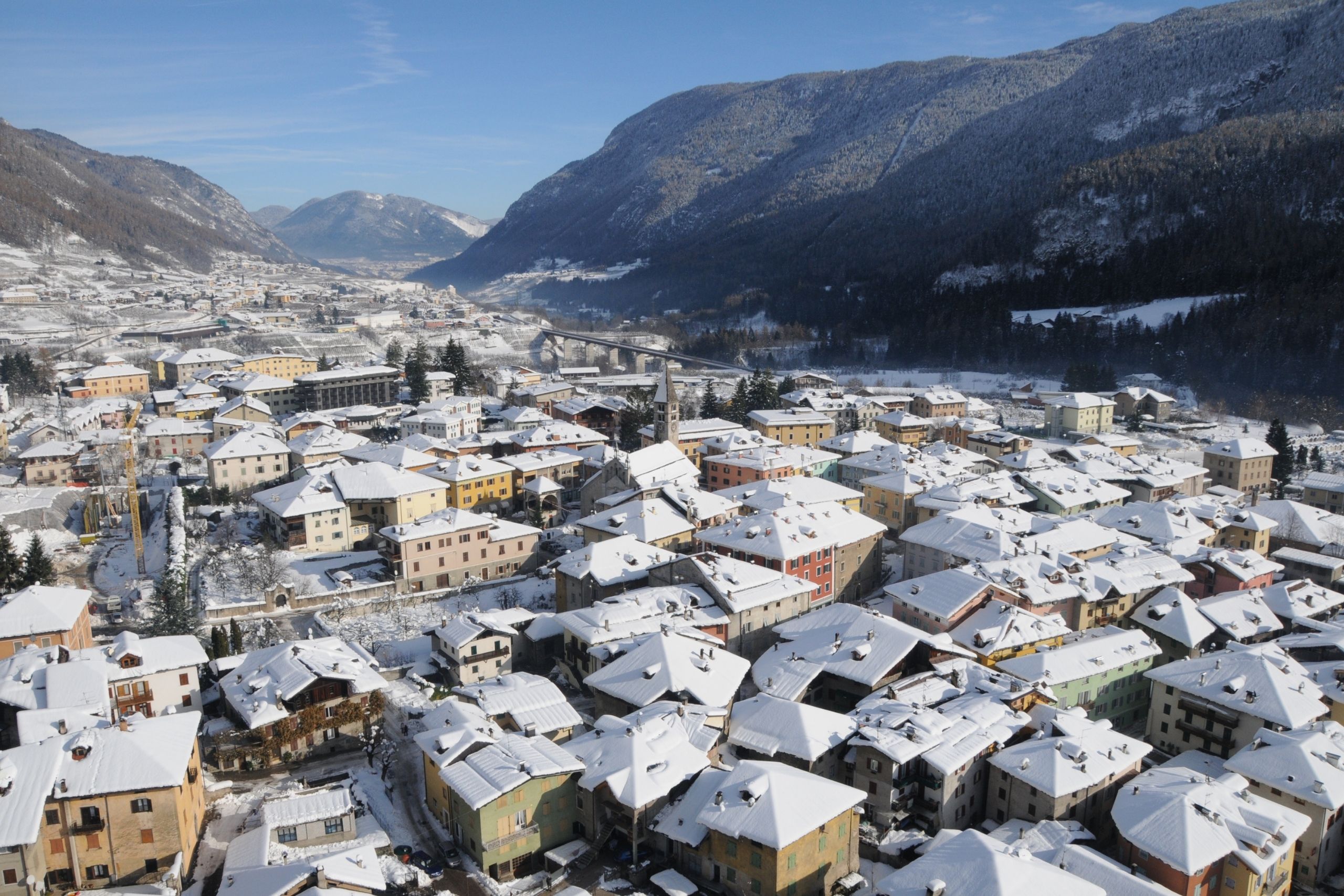 Veduta invernale di Malè: i tetti del centro coperti di neve, la chiesa e le montagne della Val di Sole